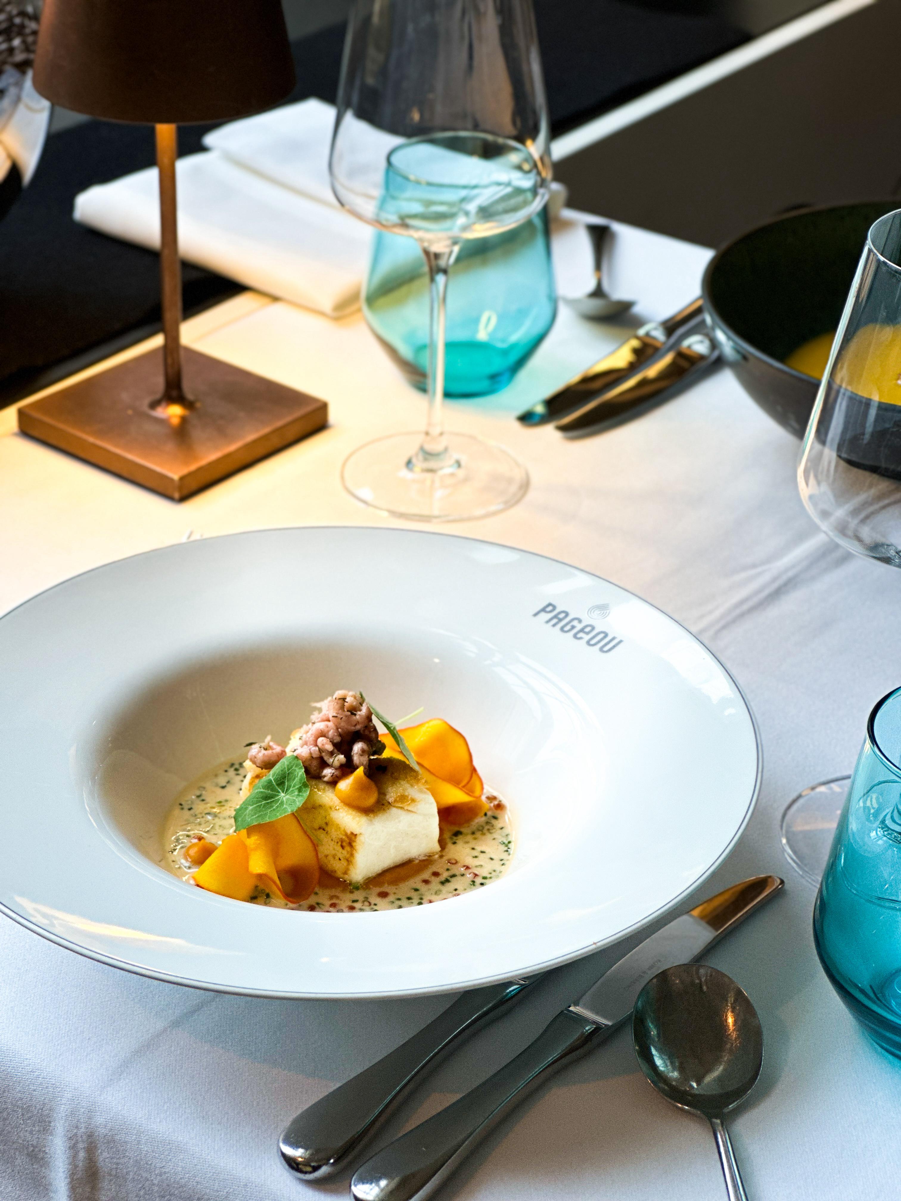 Tiefer Teller mit elegantem Fischgericht auf einem weiß gedeckten Tisch